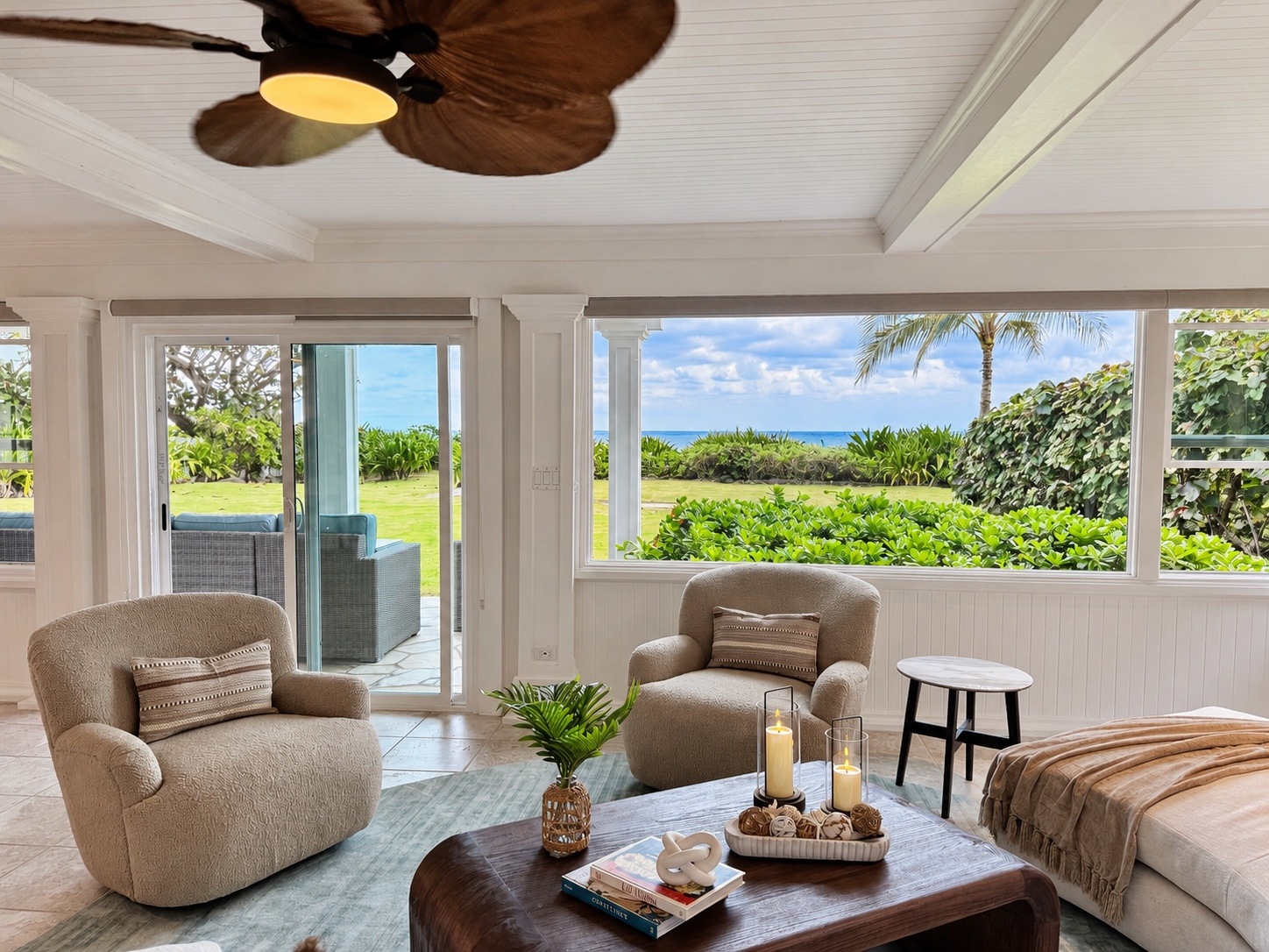Ocean-view living room with textured lounge chairs, tropical greenery and a styled coffee table